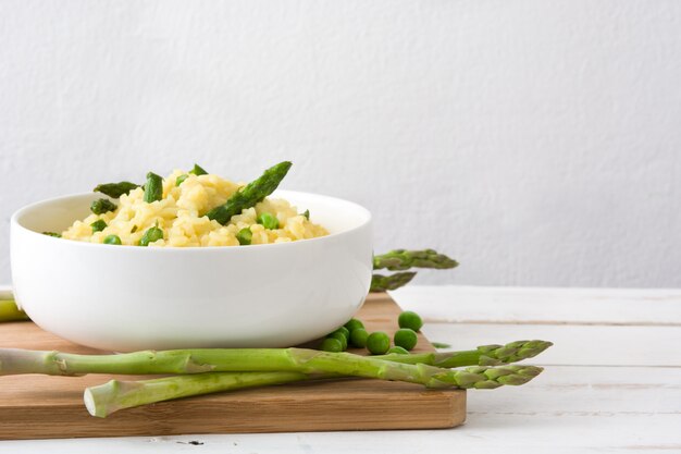 Risotto con espárragos, perejil y guisantes en un tazón de mesa de madera blanca