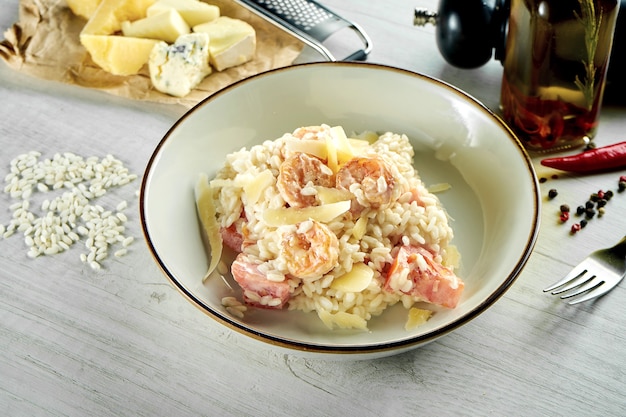 Risotto italiano clásico con queso parmesano, salsa cremosa, camarones, servido en un cuenco blanco sobre una mesa de madera. Comida de restaurante