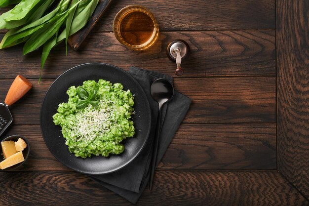 Risotto italiano Delicioso risotto con salsa de pesto o pesto de ajo silvestre albahaca queso parmesano y copa de vino blanco sobre fondo de mesa de madera antigua Cena italiana Vista superior con espacio de copia