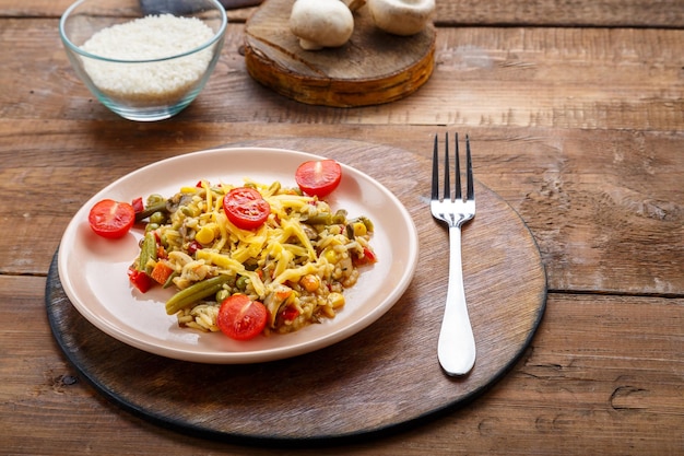 Risotto mit Biegungen und Käse auf einem Teller auf einem hölzernen Hintergrund auf einem runden Stand neben Reis