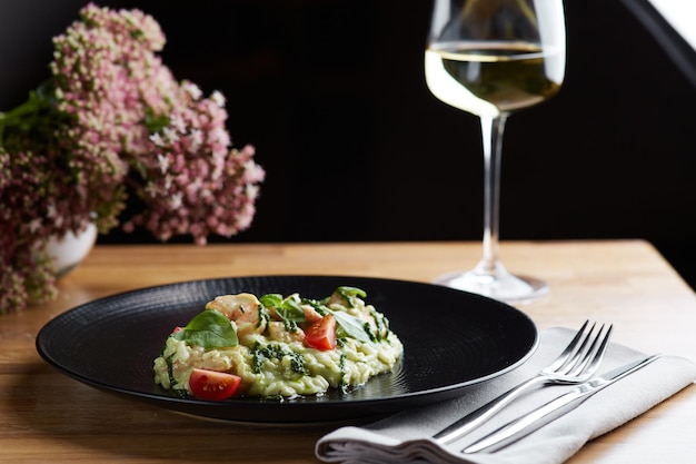 Risotto mit Pesto-Basilikum und Kirschtomaten in der Nähe auf schwarzem Teller auf Holztisch Risotto auf Holztisch Restaurant mit Glas Wein