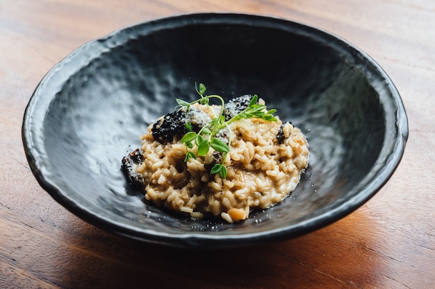 Risotto mit Pilz, frischem Kraut und Parmesankäseparmesankäse im Schwarzblech auf Holztisch.