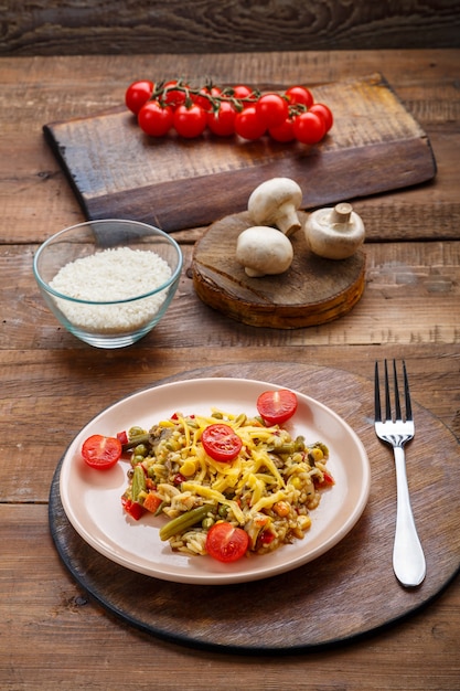 Risotto mit Pilzen in einem Teller auf Holzuntergrund auf einer Leinenserviette und einer Gabel und Zutaten.