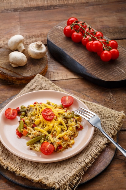 Risotto mit Rindfleisch und Käse in einem Teller auf einem hölzernen Hintergrund auf einer Serviette neben Reispilzen und Tomaten auf Brettern. Vertikales Foto