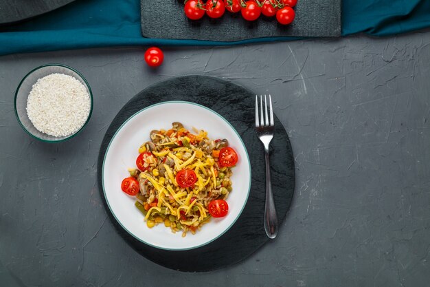 Risotto mit Rindfleisch und Käse in einem Teller auf grauem Hintergrund auf einem schwarzen Brett neben einer Gabel. Horizontales Foto