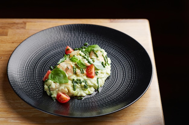 Risotto con pesto de albahaca y tomates cherry en placa negra sobre risotto de mesa de madera en restaurante de mesa de madera