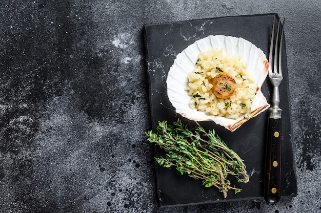 Risotto con vieiras en una concha a la sartén. Fondo negro. Vista superior. Copie el espacio.