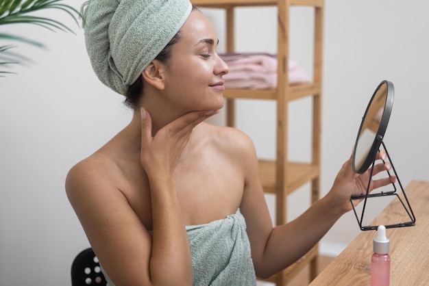 Foto ritual de beleza mulher toca pele radiante enquanto olha em um espelho redondo durante pampering cosmético