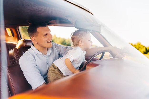 Riviera im Retro-Stil. Einzigartiges Auto. Der süße blonde Junge sitzt mit seinem Vater am Steuer eines Retro-Autos.