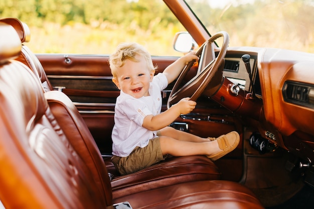 Riviera im Retro-Stil. Einzigartiges Auto. Netter blonder Junge sitzt hinter dem Lenkrad eines Retro-Autos