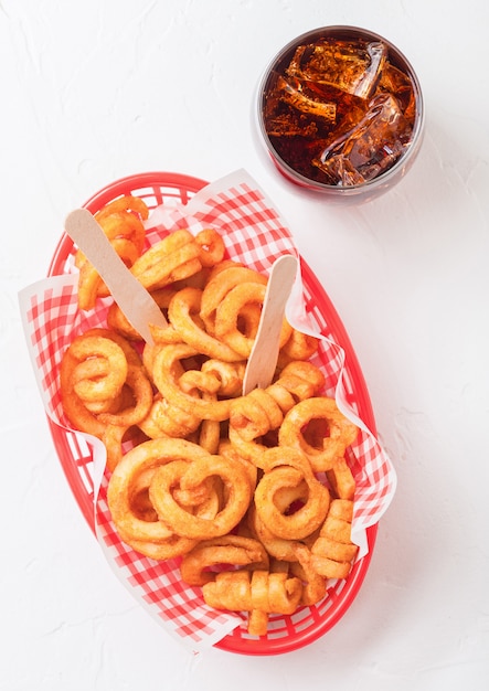 Rizado papas fritas comida rápida snack en bandeja de plástico rojo con un vaso de cola en la cocina. Comida chatarra poco saludable