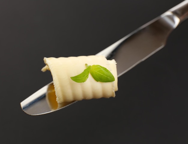 Foto rizo de mantequilla fresca con albahaca en cuchillo sobre fondo gris