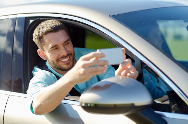 road trip, transport, reise, technologie und personenkonzept - glücklicher lächelnder mann mit smartphone, der im auto fährt und selfie macht