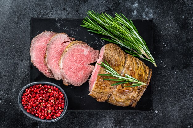 Roastbeeffilet Filetfleisch auf einem Marmorbrett. Schwarzer Hintergrund. Ansicht von oben.