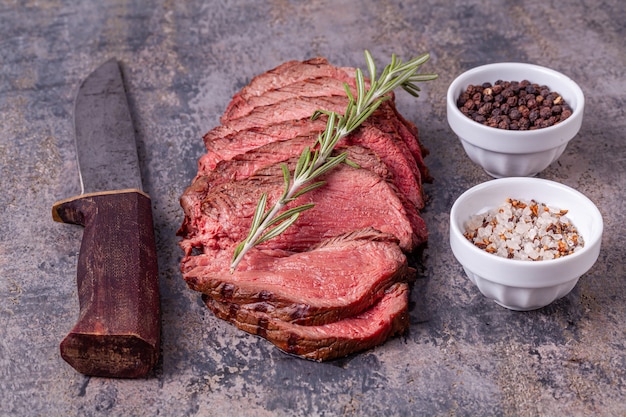 Roastbeefscheiben mit Rosmarin, Salz und Pfeffer auf grauem Marmor