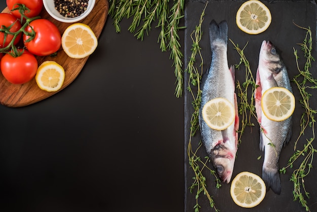 Robalo fresco, alecrim, tomate, limão, pimenta e especiarias em cima da mesa