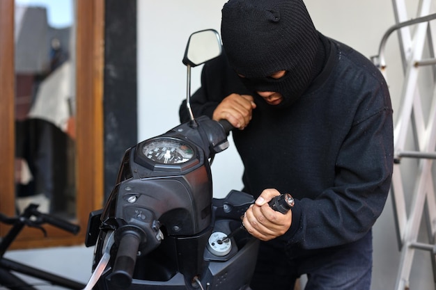 Robo de motocicletas con máscara negra usando un destornillador para romper la cerradura Concepto de crimen