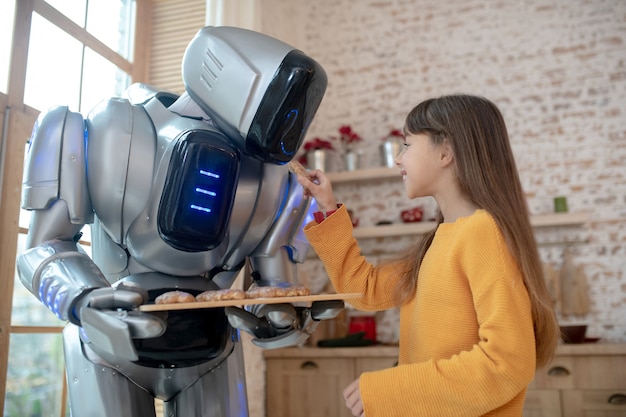 Foto robot de la casa que ofrece albóndigas a la niña sonriente en la mesa