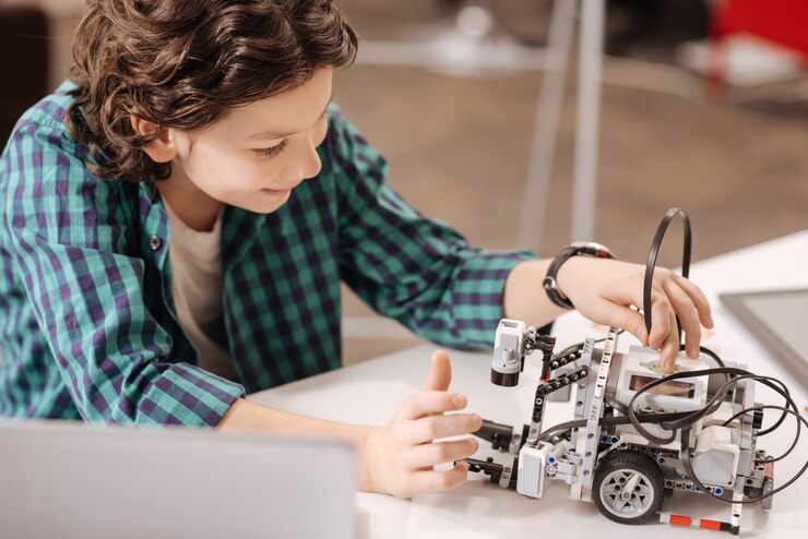 Foto robot del futuro. niño positivo encantado capaz sentado en la escuela y usando un dispositivo digital mientras estudia y expresa alegría