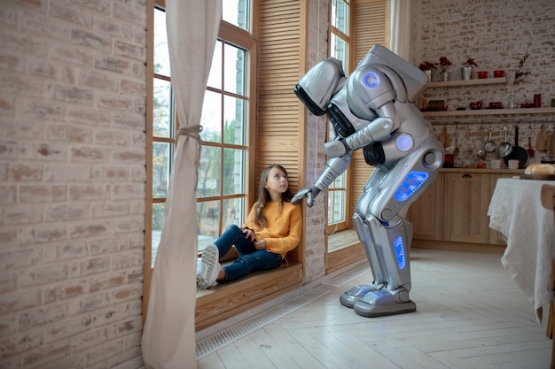 Robot hablando con la niña sentada en la ventana.