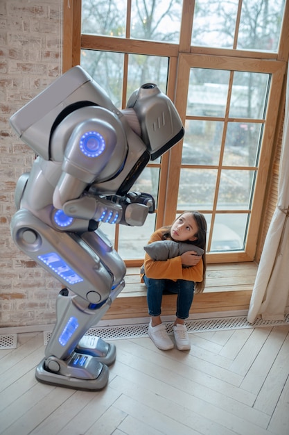 Robot hablando con la niña sentada en la ventana.