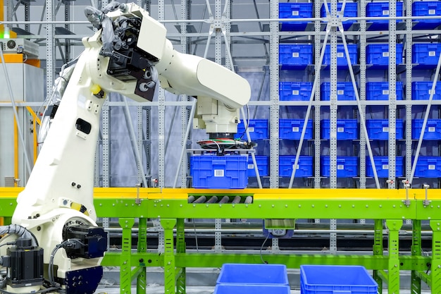 Robot industrial que se apodera del contenedor azul de la caja de plástico puesto en el transportador en almacén inteligente de la fábrica