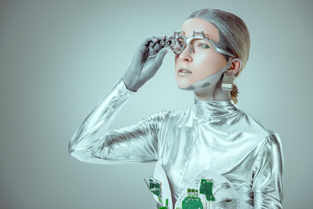 robot plateado futurista ajustando la prótesis ocular y mirando hacia otro lado aislado en el futuro gris