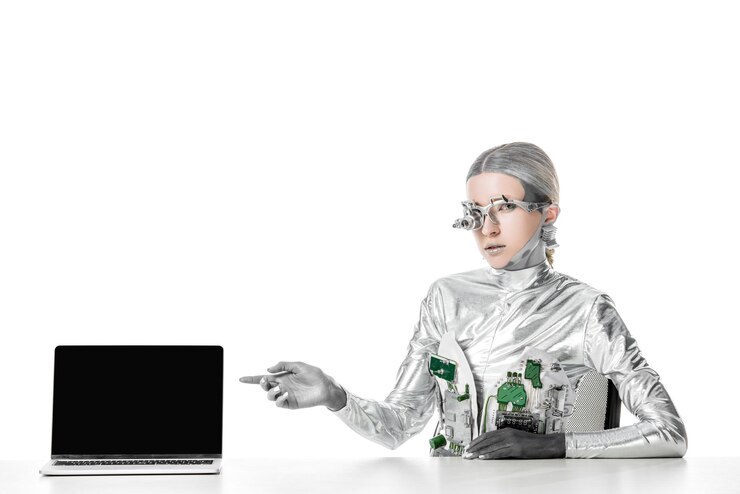 Foto robot plateado sentado en la mesa y apuntando a la computadora portátil con pantalla en blanco aislado en el futuro blanco