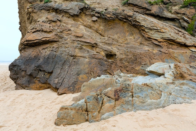 Roca estratiforme en la playa de arena y el mar detrás.