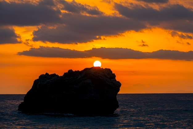 Roca solitaria en un mar en calma. Colores brillantes del atardecer en un cielo nublado