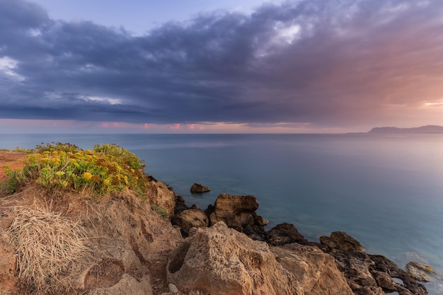 Rocas junto al mar con el telón de fondo de un colorido amanecer en un cielo nublado, Creta, Grecia