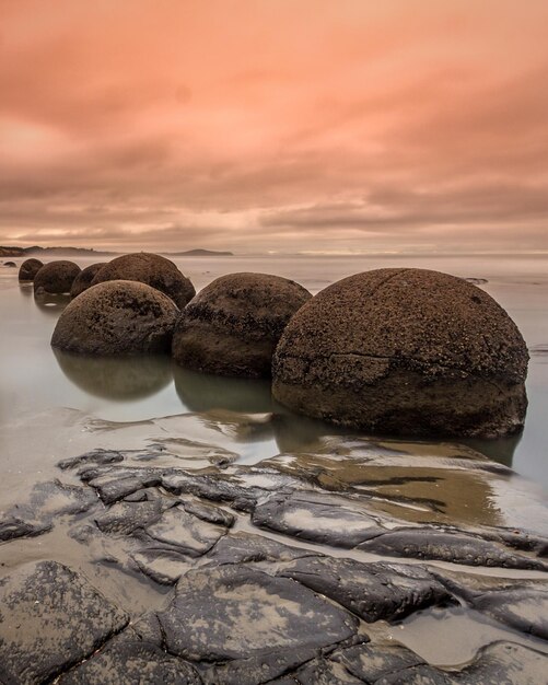 Rocas de moeraki en la orilla del mar contra el cielo nublado durante la puesta de sol