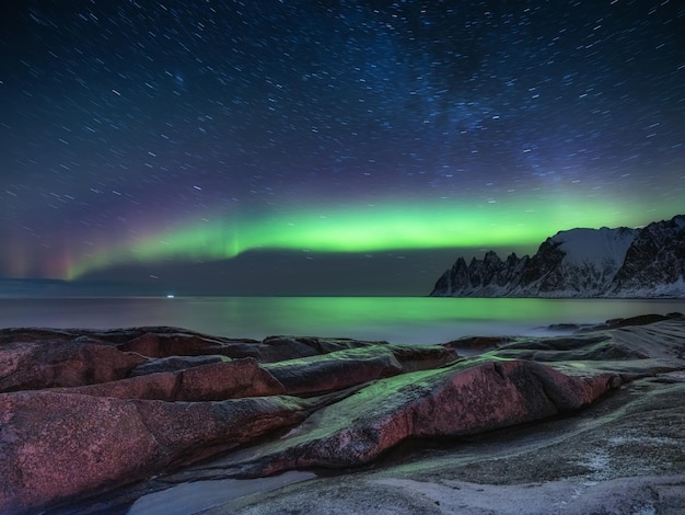 Rocas de Tungeneset y luz de aurora boreal Estelas de estrellas y aurora boreal Reflejos en la superficie del agua Islas Senja Noruega Imagen de viaje