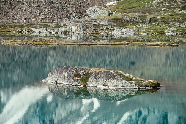 Rocha no lago turquesa da montanha. montanha nevada refletida na água clara azul do lago glacial. fundo bonito e ensolarado com reflexo glaciar branco como a neve na superfície da água verde do lago de montanha.