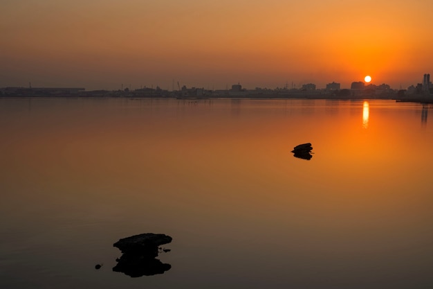 Rochas com reflexões na água calma e nascer do sol bonito sobre o céu colorido com fundo da silhueta, Barém.