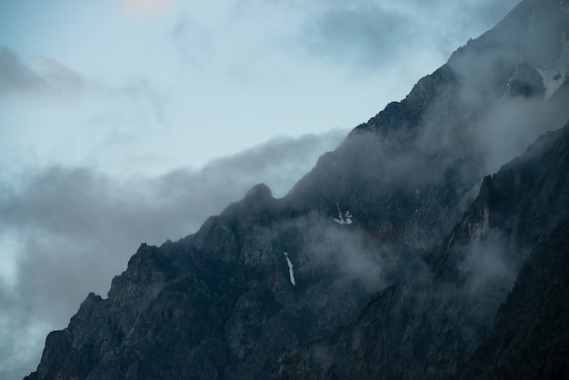 Rochas gigantes fantasmagóricas com árvores no meio do nevoeiro. misteriosa montanha enorme com neve na névoa. de manhã cedo nas montanhas. nevoeiro impenetrável. paisagem misteriosa atmosférica escura. atmosfera mística tranquila.