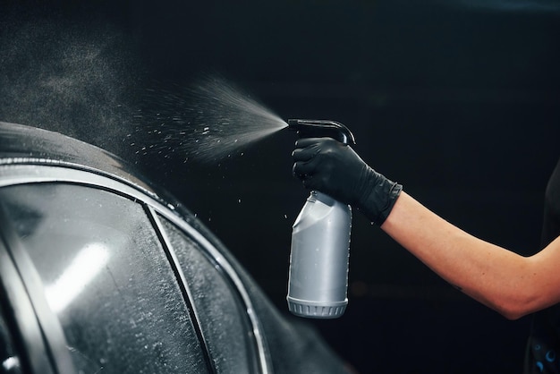 Rociar el vehículo Automóvil negro moderno limpiado por una mujer dentro de la estación de lavado de autos