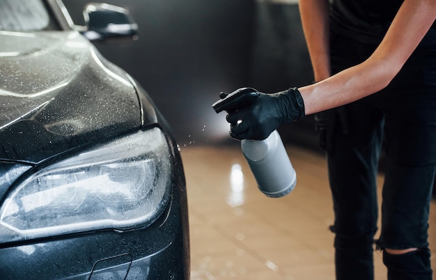 Rociar el vehículo Automóvil negro moderno limpiado por una mujer dentro de la estación de lavado de autos