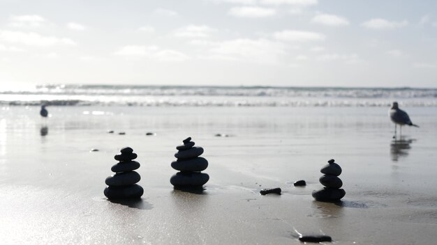 Rock balancieren am ozeanstrand, steine stapeln sich durch meerwasserwellen. pyramide von kieselsteinen am sandigen ufer. stabiler haufen oder haufen im weichzeichner mit bokeh, nahaufnahme. nahtloser geloopter cinemagraph. zen-balance.