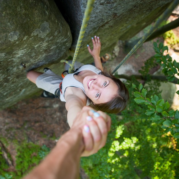 Rockclimber segurando alpinista feminina com a mão em uma parede rochosa