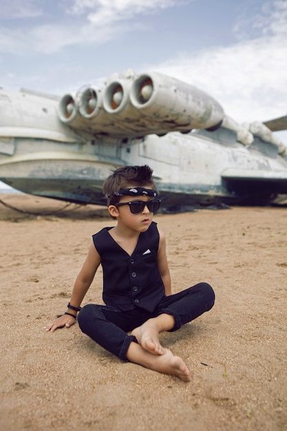 Rocker boy un niño vestido de negro se encuentra en el contexto de un avión abandonado en la playa