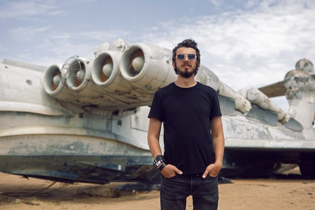 Rocker-Mann in schwarzer Kleidung steht vor dem Hintergrund eines verlassenen Flugzeugs am Strand