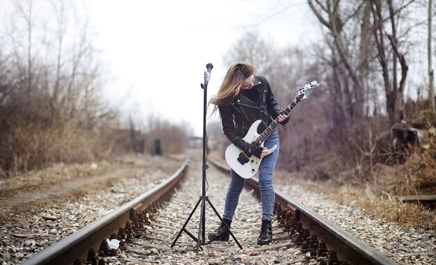 Rockero hermosa joven con guitarra eléctrica. Canta una chica músico de rock con una chaqueta de cuero con una guitarra. Un solista de una banda de rock toca la guitarra y grita por el micrófono.