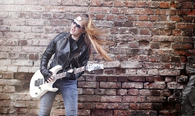 Rockero hermosa joven con guitarra eléctrica. Canta una chica músico de rock con una chaqueta de cuero con una guitarra. Un solista de una banda de rock toca la guitarra y grita por el micrófono.