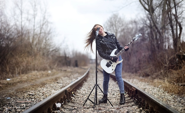 Rockero hermosa joven con guitarra eléctrica. Canta una chica músico de rock con una chaqueta de cuero con una guitarra. Un solista de una banda de rock toca la guitarra y grita por el micrófono.