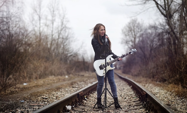 Rockero hermosa joven con guitarra eléctrica. Canta una chica músico de rock con una chaqueta de cuero con una guitarra. Un solista de una banda de rock toca la guitarra y grita por el micrófono.