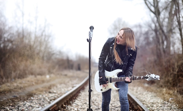 Rockero hermosa joven con guitarra eléctrica. Canta una chica músico de rock con una chaqueta de cuero con una guitarra. Un solista de una banda de rock toca la guitarra y grita por el micrófono.