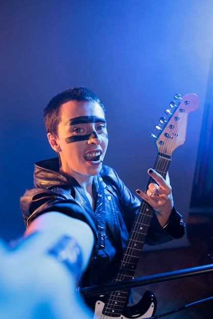 Rockero punk mostrando signos de rock en cámara y tocando guitarra, creando actuaciones musicales y actuando como locos. Artista que produce música alternativa de heavy metal con instrumento, actuación en vivo.