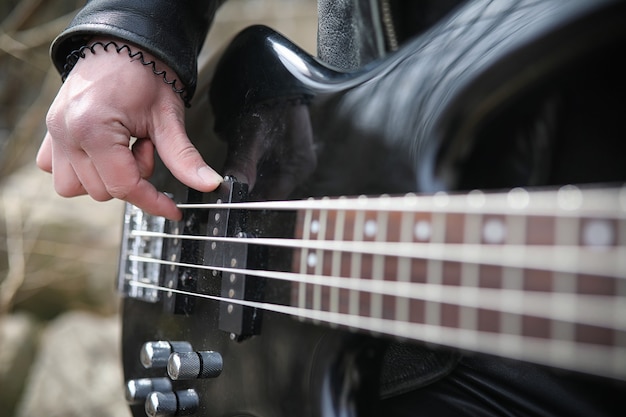 Rockgitarrist auf den Stufen. Ein Musiker mit Bassgitarre im Lederanzug. Metalist mit Gitarre auf dem Hintergrund des Industrieschritts.