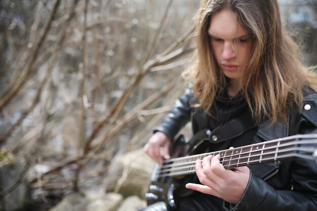 Rockgitarrist auf den Stufen. Ein Musiker mit einer Bassgitarre in einem Lederanzug. Metalist mit Gitarre vor dem Hintergrund des Industrieschritts.